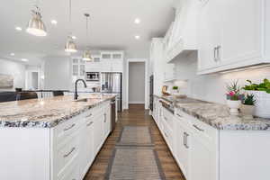 Kitchen with white cabinets, hanging light fixtures, glass insert cabinets, a kitchen island with sink, and light stone counters