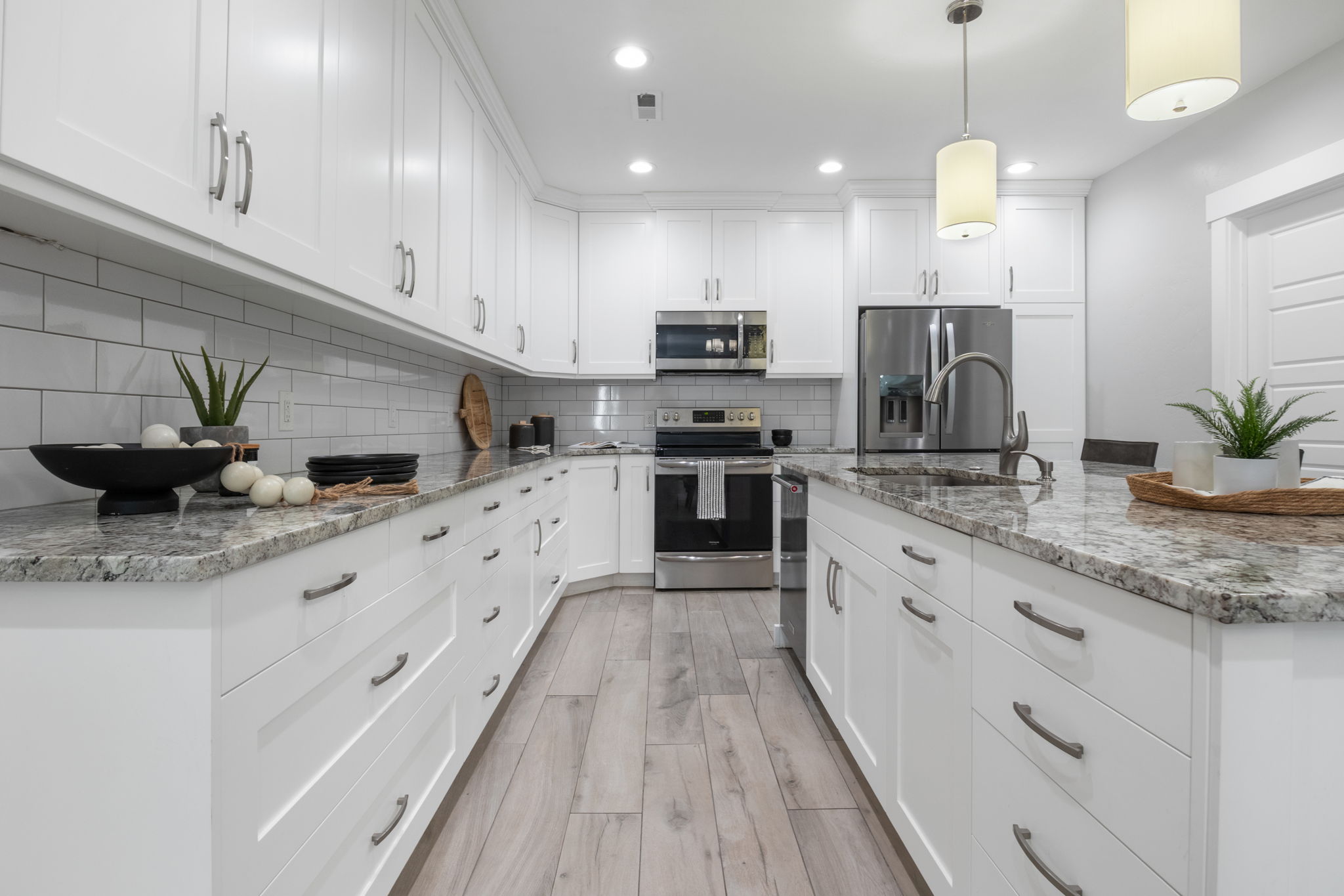 Full kitchen with white cabinets, light stone countertops, stainless steel appliances, and light wood-type flooring
