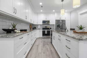 Full kitchen with white cabinets, light stone countertops, stainless steel appliances, and light wood-type flooring