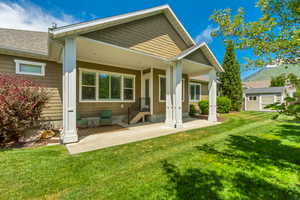 Expansive lawn with a covered patio, featuring substantial white support columns, a gray shingle roof, and a visible mountain backdrop