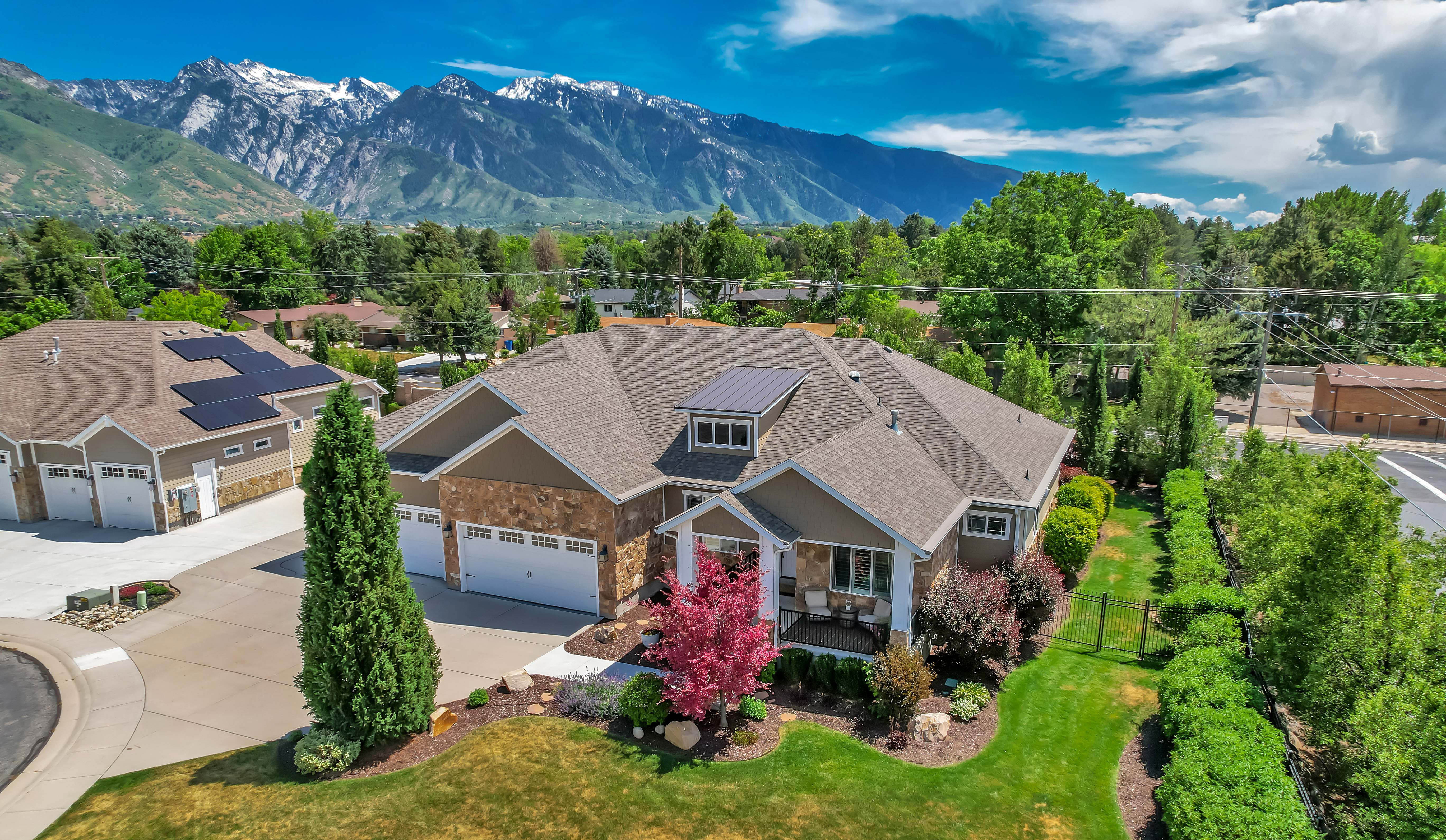 Contemporary residence featuring a multi-car garage, stone and siding exterior, dormer windows, and mature landscaping