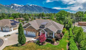 Contemporary residence featuring a multi-car garage, stone and siding exterior, dormer windows, and mature landscaping