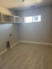 Laundry area featuring a textured ceiling, hookup for an electric dryer, and light wood-type flooring