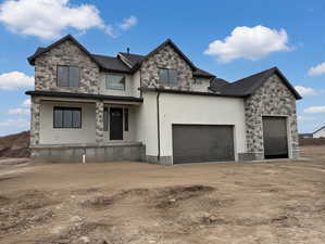 View of front of house with stone siding, driveway, an attached garage, and covered porch
