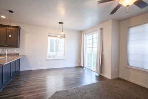 Unfurnished dining area with ceiling fan, dark wood-style floors, and a textured ceiling
