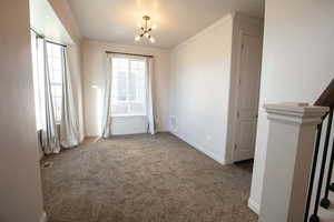 Empty room with crown molding, light carpet, a chandelier, and a textured ceiling