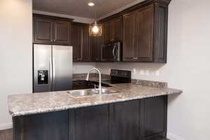 Kitchen featuring stainless steel appliances, dark wood finish cabinets, a peninsula, decorative light fixtures, and a textured ceiling