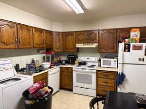 Kitchen featuring light floors, washer / clothes dryer, white appliances, light countertops, and wood finish cabinetry