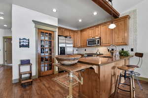 Kitchen with a peninsula, a breakfast bar area, wood finish cabinetry, stainless steel appliances, and hanging light fixtures