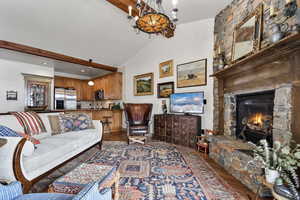 Living area featuring dark wood-style floors, a stone fireplace, and vaulted ceiling