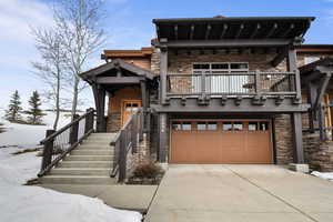 View of front of house featuring stone siding, a garage, concrete driveway, and a balcony