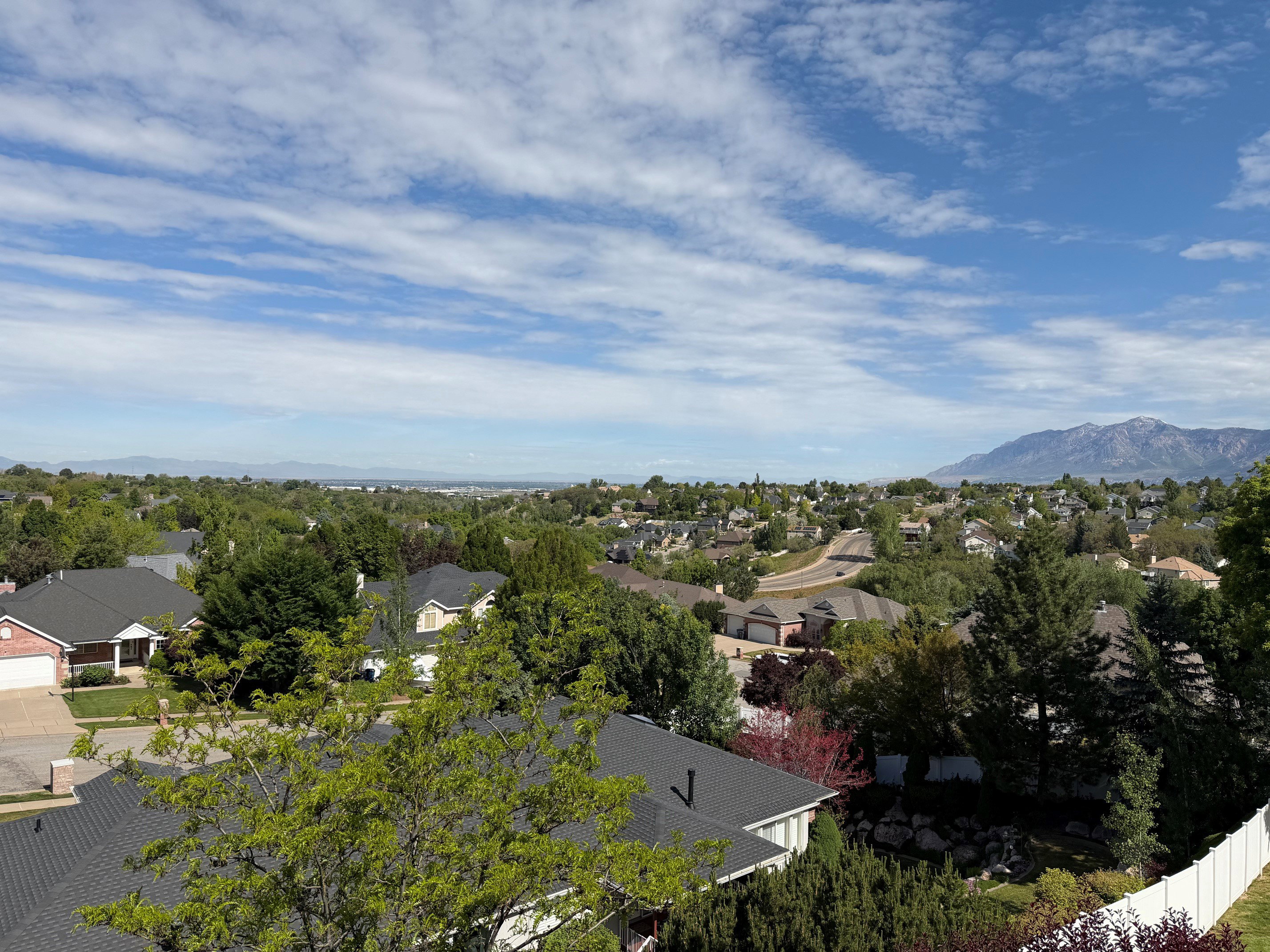 Expansive mountain backdrop with a visible neighborhood featuring residential rooftops, mature trees, and varying terrain