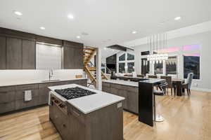 Kitchen with a kitchen island, stainless steel gas stovetop, modern cabinets, light wood-type flooring, and dark wood finish cabinetry