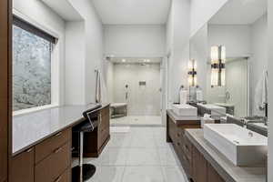 Bathroom with double vanity, a marble finish shower, and light marble finish flooring