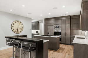 Kitchen with recessed lighting, light wood-style floors, built in appliances, dark stone countertops, and a breakfast bar