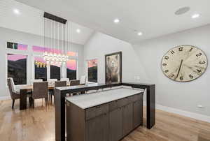 Kitchen featuring suspended lighting, dark wood finish cabinetry, light wood-type flooring, a center island, and vaulted ceiling