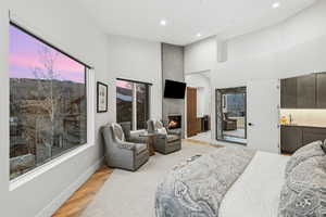 Bedroom featuring light wood-type flooring, a large fireplace, a high ceiling, recessed lighting, and ensuite bath