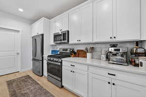 Kitchen featuring stainless steel appliances, white cabinetry, light wood-style flooring, light stone countertops, and tasteful backsplash