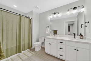 Full bath with double vanity, a shower with shower curtain, and wood finish floors