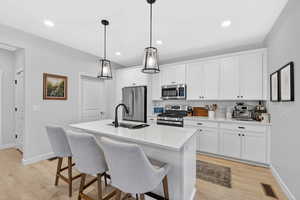 Kitchen with stainless steel appliances, white cabinetry, a kitchen bar, light wood-style floors, and a kitchen island with sink