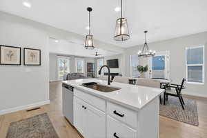 Kitchen featuring white cabinets, open floor plan, a center island with sink, light wood-type flooring, and stainless steel dishwasher