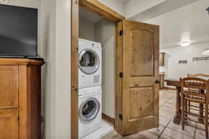 Laundry area with stacked washer and clothes dryer and light tile patterned flooring