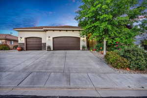 View of front facade with stucco siding, a garage, stone siding, and concrete driveway