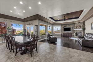 Tiled dining room with a raised ceiling, a stone fireplace, and a ceiling fan