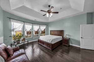 Bedroom with dark wood-style flooring, a ceiling fan, and a raised ceiling