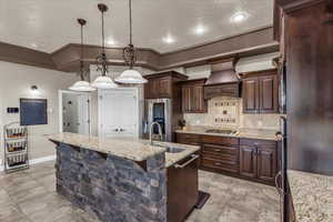 Kitchen with dark wood finish cabinets, an island with sink, pendant lighting, and light stone countertops