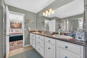 Bathroom featuring double vanity, a shower stall, light tile patterned flooring, connected bathroom, and suspended lighting