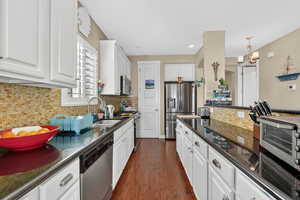 Kitchen featuring decorative backsplash, white cabinetry, stainless steel appliances, dark wood-style flooring, and dark stone counters