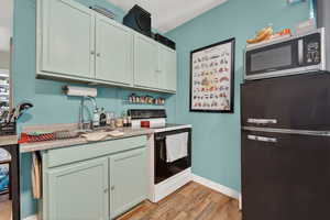 Kitchen featuring range with electric cooktop, freestanding refrigerator, stainless steel microwave, and light wood finished floors