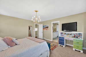 Bedroom with connected bathroom, light carpet, and suspended lighting