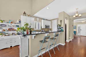 Kitchen featuring a kitchen breakfast bar, arched walkways, white cabinetry, and dark wood-type flooring