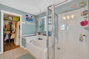 Bathroom featuring tile patterned flooring, a shower stall, a walk in closet, and a garden tub
