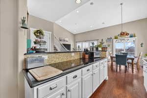 Kitchen featuring white cabinetry, pendant lighting, dark wood finished floors, vaulted ceiling, and dark stone countertops