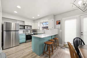 Dual tone kitchen featuring stainless steel appliances, dual tone cabinetry, light countertops, a kitchen bar, and light wood-style floors