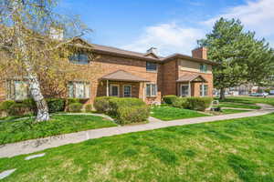 View of front of property featuring a chimney, brick siding, and a front yard
