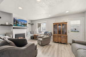 Living area featuring a glass covered fireplace, recessed lighting, light wood-style floors, and a textured ceiling