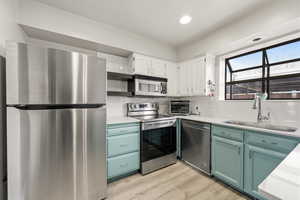 Kitchen with stainless steel appliances, dual tone cabinetry, light countertops, light wood-style flooring, and recessed lighting