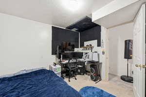Bedroom featuring light colored carpet, a desk, and a textured ceiling