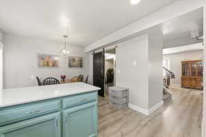 Kitchen with a barn door, light wood-style flooring, suspended lighting, and light stone counters