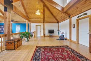 Living room featuring light wood finished floors, a high wooden beamed ceiling, and a ceiling fan