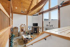 Rec room featuring a ceiling fan, stone finish floors, a high wood beamed ceiling, and a stone fireplace
