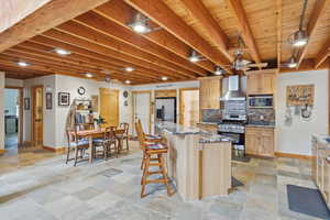 Kitchen featuring stone tile flooring, stainless steel appliances, a ceiling fan, light wood finish cabinetry, and dark stone countertops