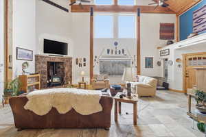 Living area featuring ceiling fan, a wood stove, and a high ceiling