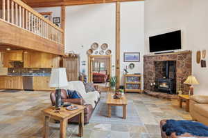 Living room featuring a wood stove, light stone finish floors, and lofted ceiling