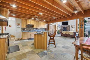 Kitchen featuring a breakfast bar area, dark stone countertops, a fireplace, open floor plan, and a ceiling fan