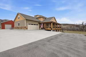 View of front of house featuring a porch, stone siding, roof with shingles, driveway, and a garage